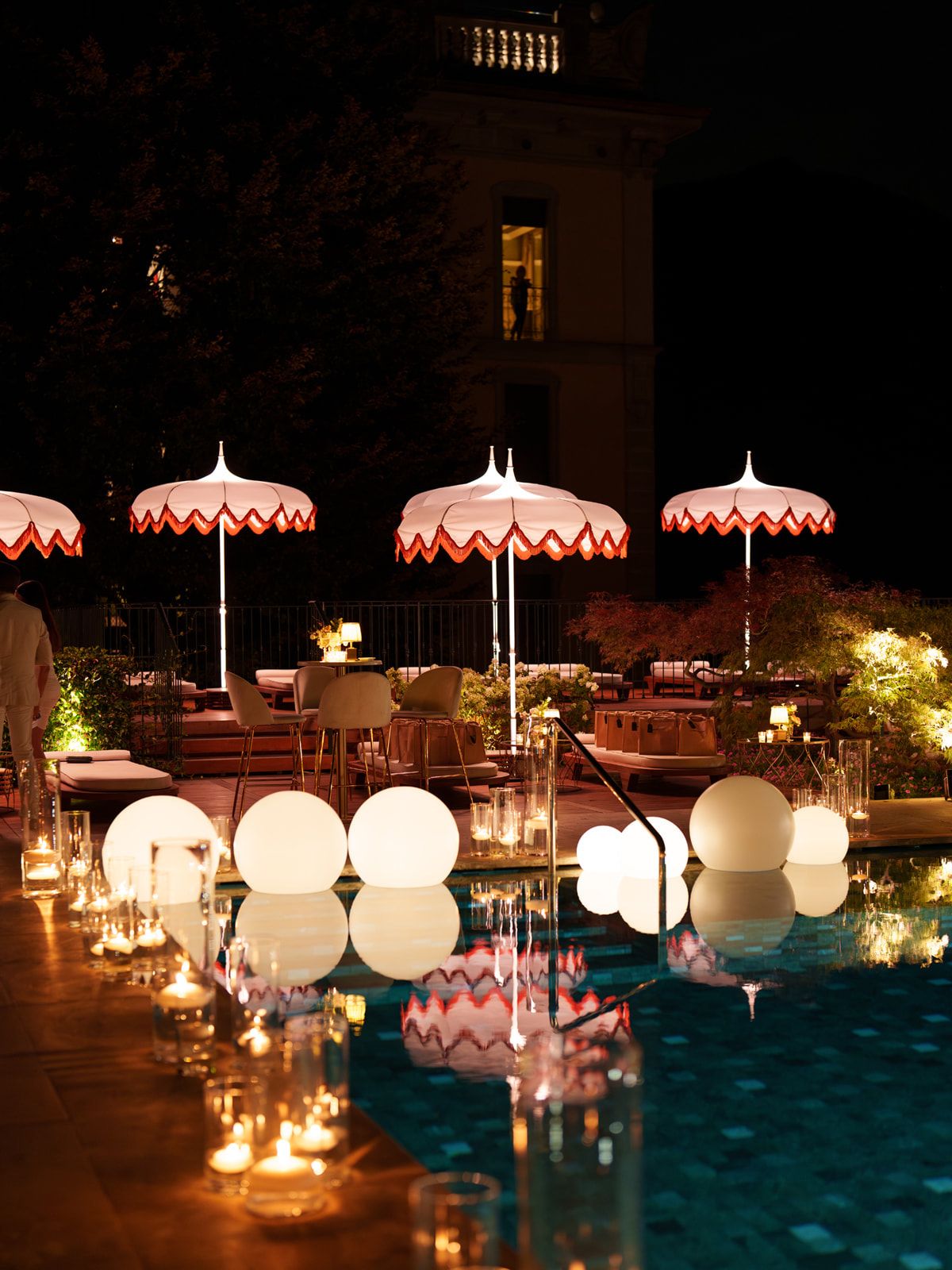 An intimate evening poolside setting with sculptural white lights, candles and scalloped umbrellas